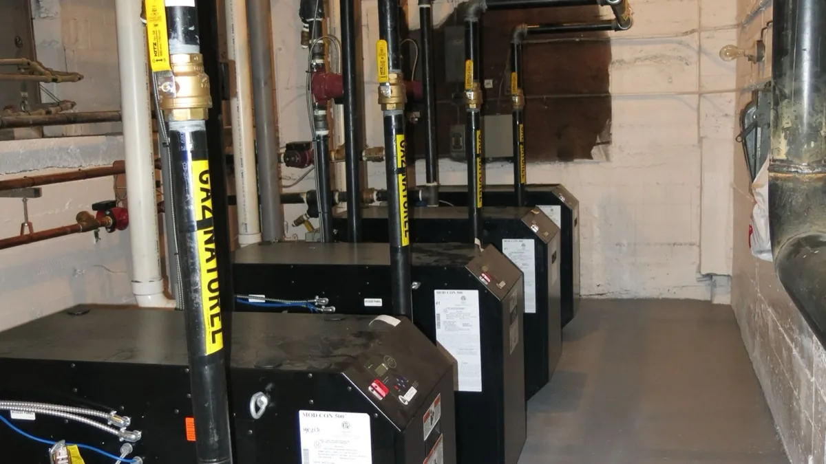 Black steel natural-gas distribution pipes feeding multiple boilers in a mechanical room